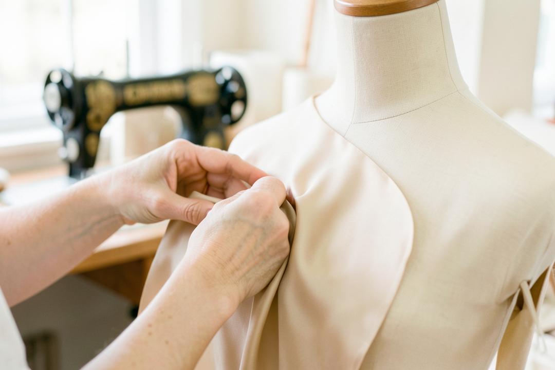 Hands pinning bone-coloured silk on a dress form in the Barzezzi atelier